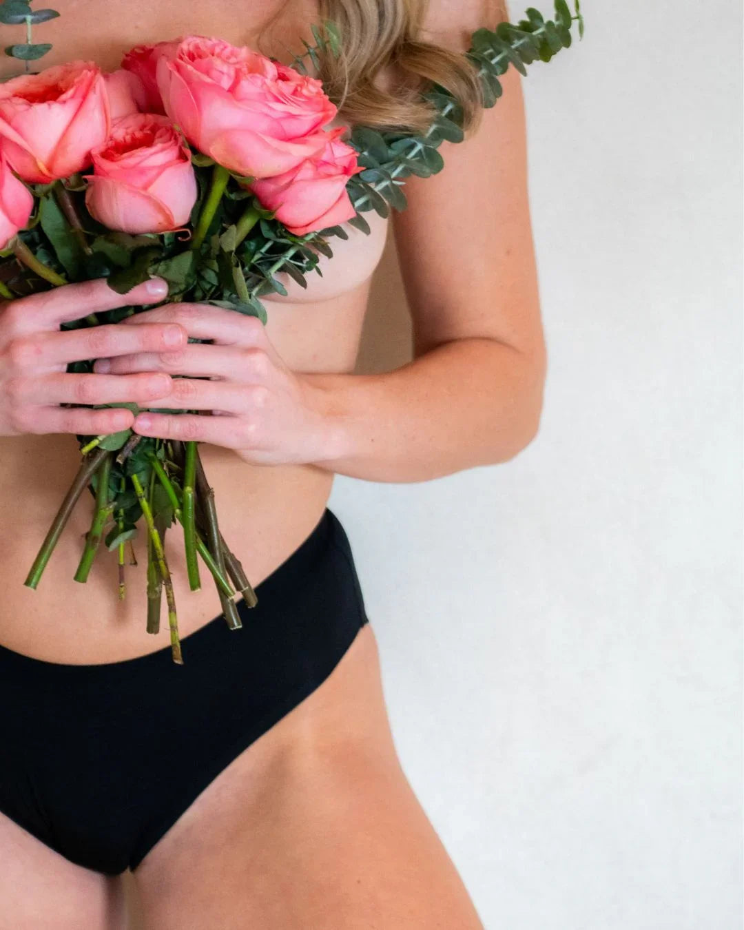 Woman wearing black period underwear holding pink roses and eucalyptus stems