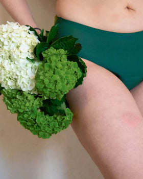 Close-up of a woman wearing green Heralogie period underwear holding a bouquet of white and green hydrangeas, symbolizing natural feminine care and sustainability.