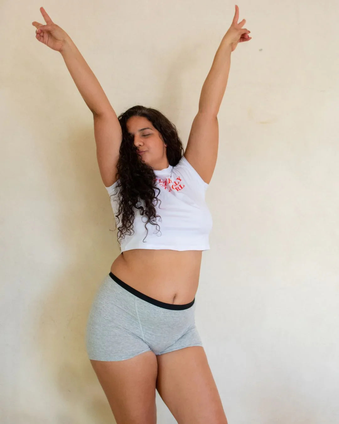 Woman in gray period underwear and white crop top posing confidently against a neutral background.
