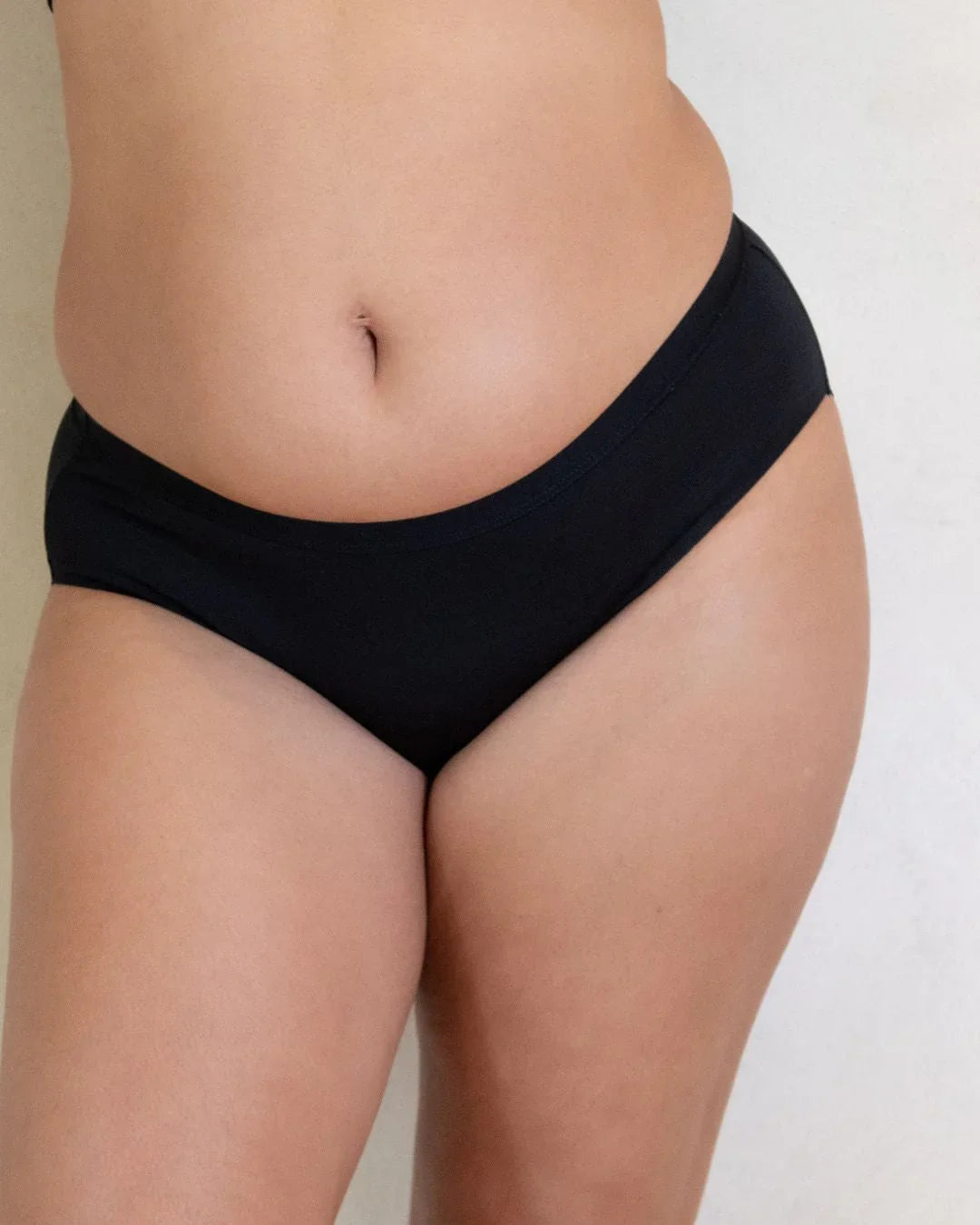 Woman wearing black, leak-proof period underwear against a neutral background